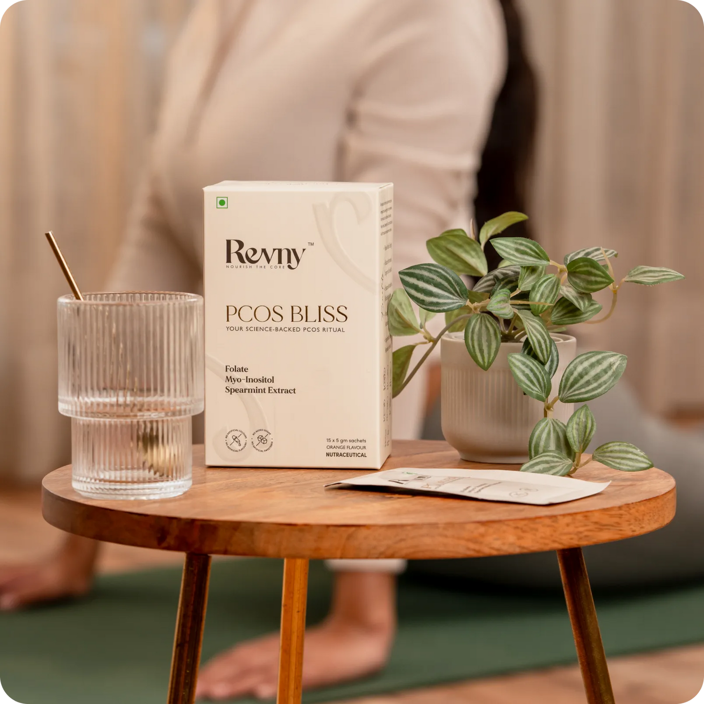 Revmy PCOS Bliss product box on a wooden table with a plant and glass.