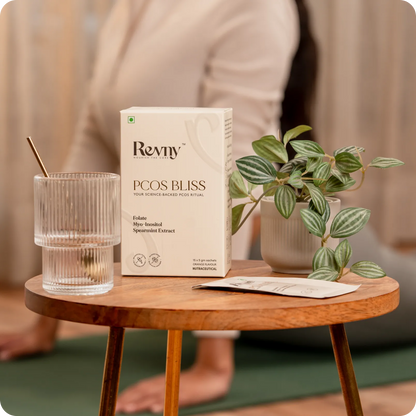 Revmy PCOS Bliss product box on a wooden table with a plant and glass.